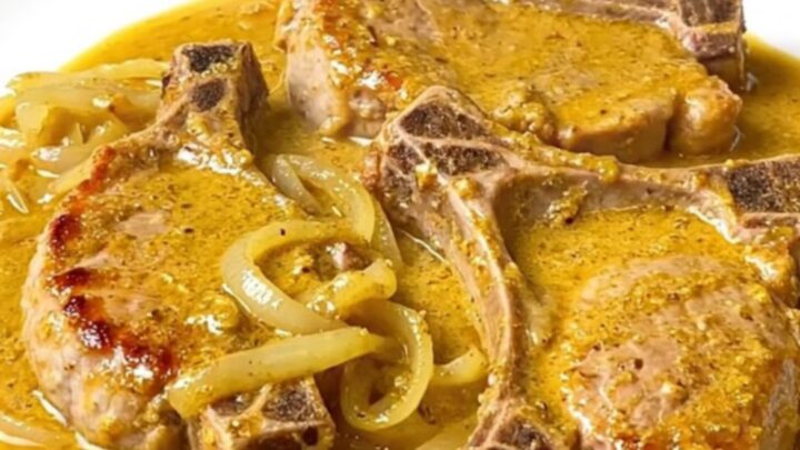 A close-up of tender, braised pork chops covered in a creamy, golden beer and cheddar cheese sauce on a white plate.
