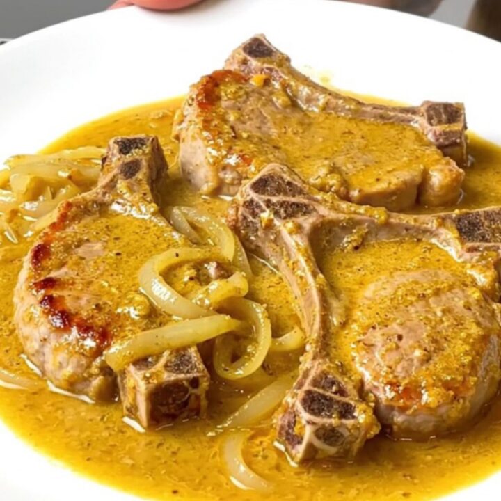 A close-up of tender, braised pork chops covered in a creamy, golden beer and cheddar cheese sauce on a white plate.