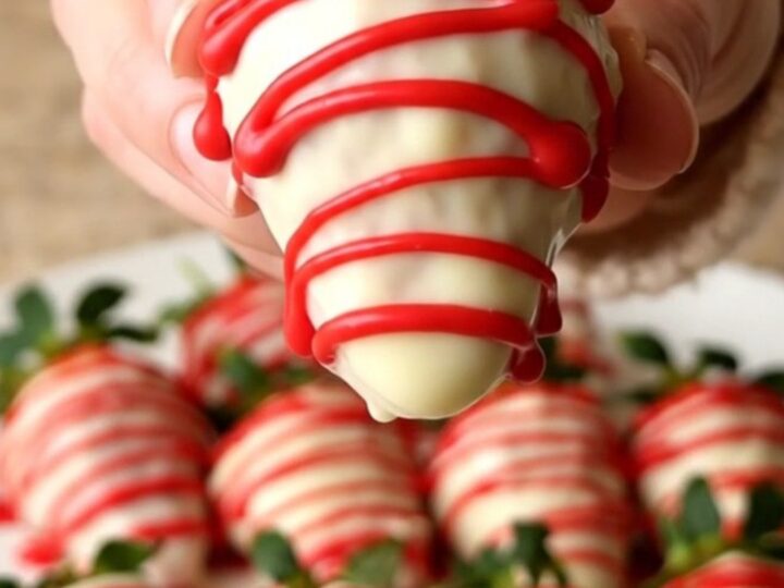 A tray of fresh strawberries dipped in white chocolate with a red candy drizzle.