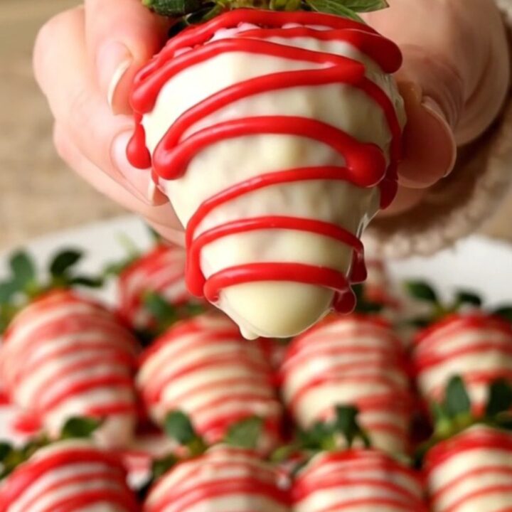A tray of fresh strawberries dipped in white chocolate with a red candy drizzle.