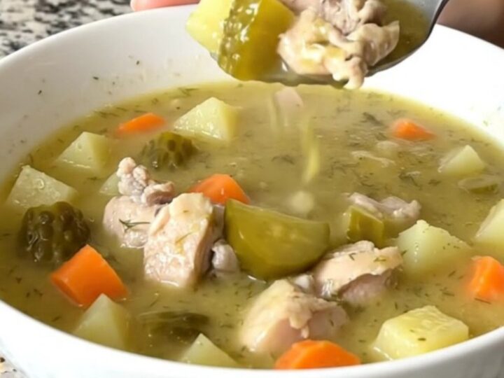 A white bowl filled with creamy dill pickle chicken soup, featuring visible chunks of chicken, potatoes, and pickles.