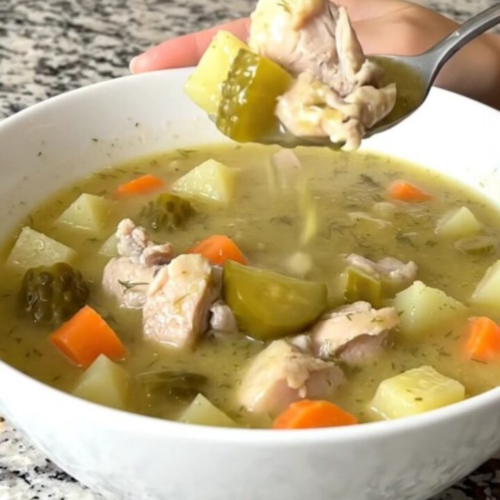 A white bowl filled with creamy dill pickle chicken soup, featuring visible chunks of chicken, potatoes, and pickles.