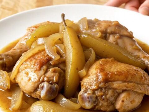 A close-up of tender, slow-cooked chicken thighs topped with soft, spiced pears and onions in a stainless steel slow cooker.