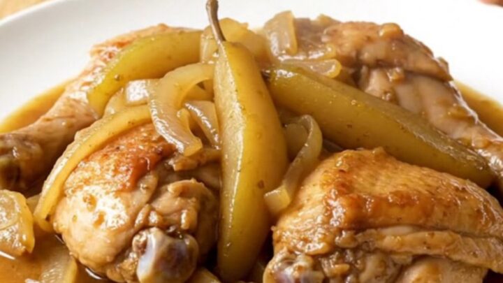 A close-up of tender, slow-cooked chicken thighs topped with soft, spiced pears and onions in a stainless steel slow cooker.