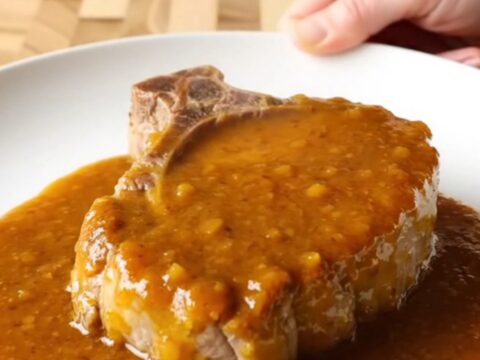 A close-up of a slow-cooked, tender boneless pork chop coated in a rich, amber apricot BBQ sauce on a plate.