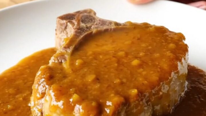 A close-up of a slow-cooked, tender boneless pork chop coated in a rich, amber apricot BBQ sauce on a plate.