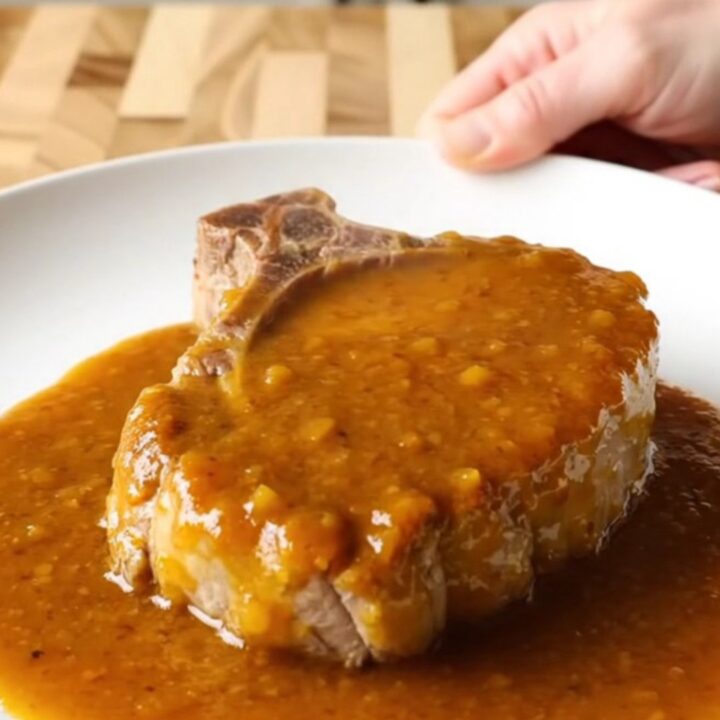 A close-up of a slow-cooked, tender boneless pork chop coated in a rich, amber apricot BBQ sauce on a plate.