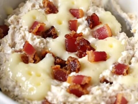 A creamy chicken bacon Swiss dip in a black slow cooker with a spoon ready to serve.
