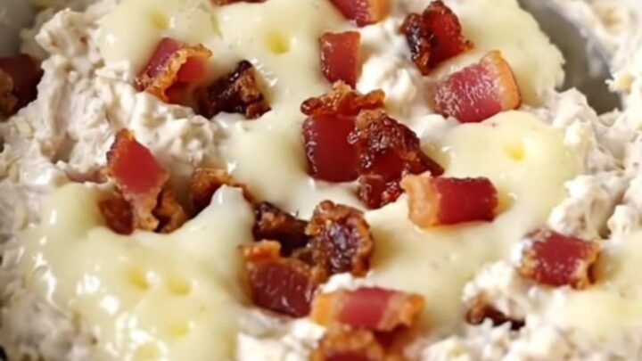 A creamy chicken bacon Swiss dip in a black slow cooker with a spoon ready to serve.