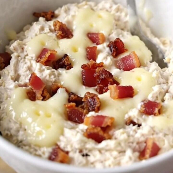 A creamy chicken bacon Swiss dip in a black slow cooker with a spoon ready to serve.