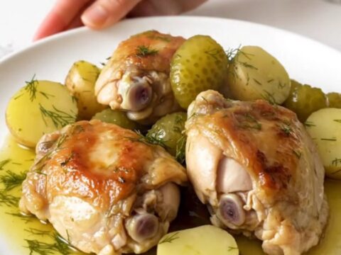 A close-up of tender chicken thighs and soft potatoes in a creamy dill sauce inside a black slow cooker.