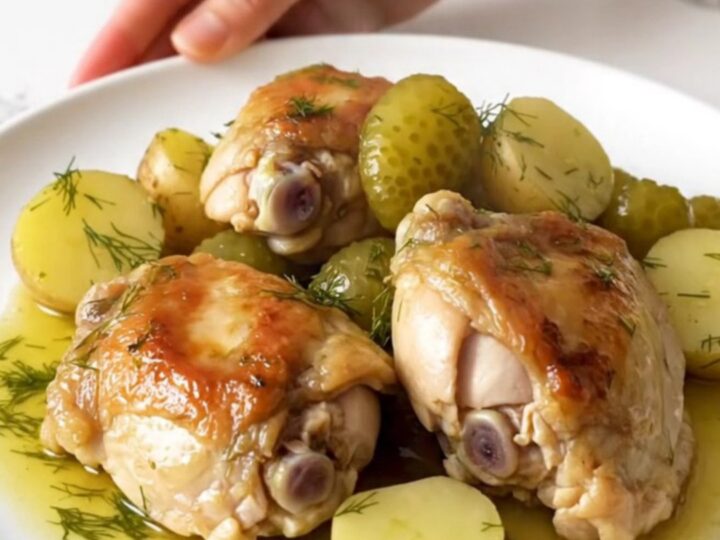 A close-up of tender chicken thighs and soft potatoes in a creamy dill sauce inside a black slow cooker.