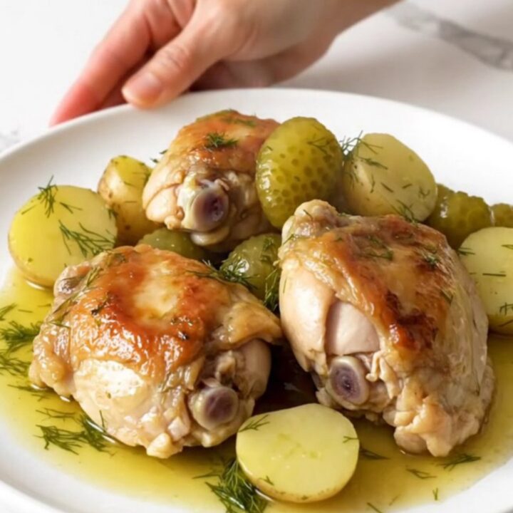 A close-up of tender chicken thighs and soft potatoes in a creamy dill sauce inside a black slow cooker.