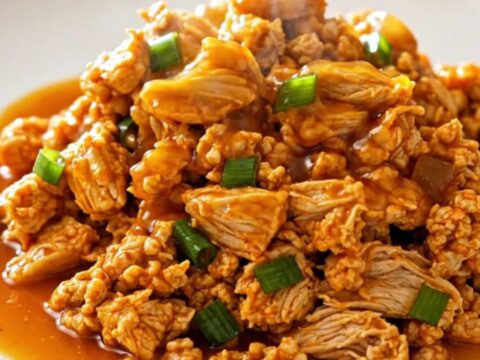 A close-up of slow cooker orange ground turkey served in a white bowl with green onions.