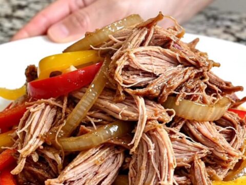 A slow cooker filled with tender pulled pork, colorful bell peppers, and onions in a rich, flavorful sauce.