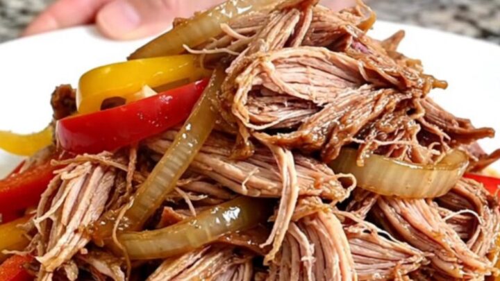 A slow cooker filled with tender pulled pork, colorful bell peppers, and onions in a rich, flavorful sauce.