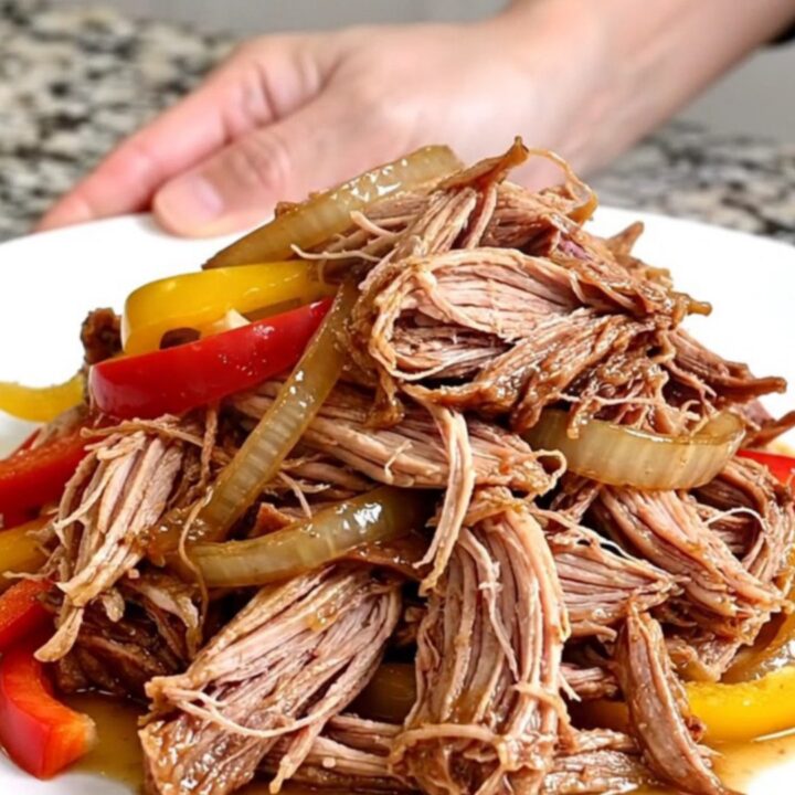 A slow cooker filled with tender pulled pork, colorful bell peppers, and onions in a rich, flavorful sauce.