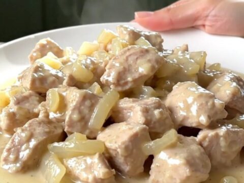 A top-down view of tender chicken breast chunks in a rich, creamy white sauce inside a black slow cooker.