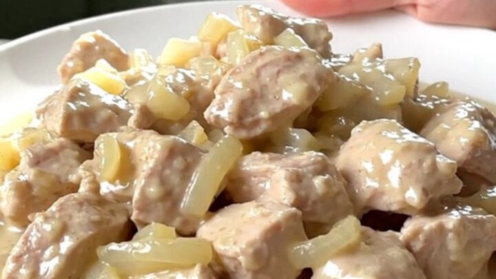 A top-down view of tender chicken breast chunks in a rich, creamy white sauce inside a black slow cooker.