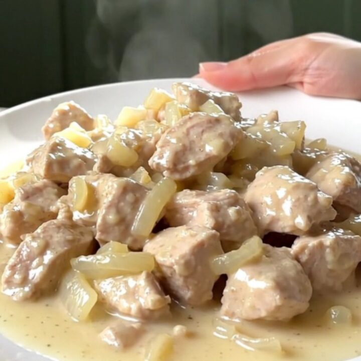 A top-down view of tender chicken breast chunks in a rich, creamy white sauce inside a black slow cooker.