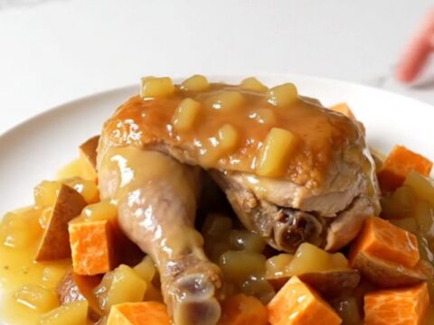 A top-down view of raw chicken breasts, sweet potato cubes, and apple slices in a slow cooker insert.