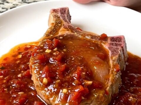 A serving spoon lifts a tender, saucy boneless pork chop from a slow cooker filled with chunky salsa.