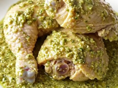 A close-up of tender chicken thighs covered in a creamy, vibrant green salsa verde sauce in a black slow cooker.