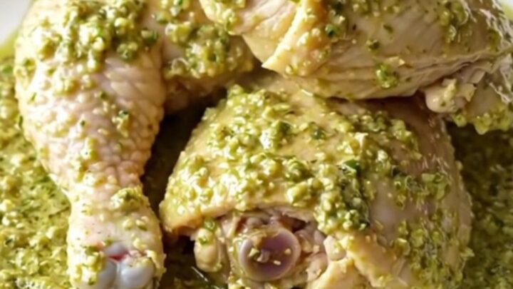 A close-up of tender chicken thighs covered in a creamy, vibrant green salsa verde sauce in a black slow cooker.