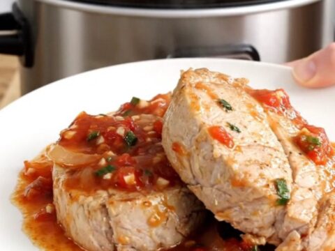 A slow cooker filled with pork tenderloin, sliced bell peppers, and onions in a rich salsa sauce, ready for serving.