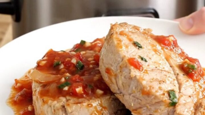 A slow cooker filled with pork tenderloin, sliced bell peppers, and onions in a rich salsa sauce, ready for serving.