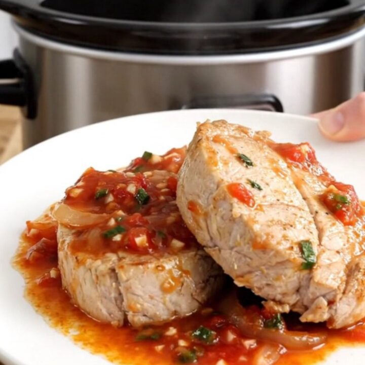 A slow cooker filled with pork tenderloin, sliced bell peppers, and onions in a rich salsa sauce, ready for serving.