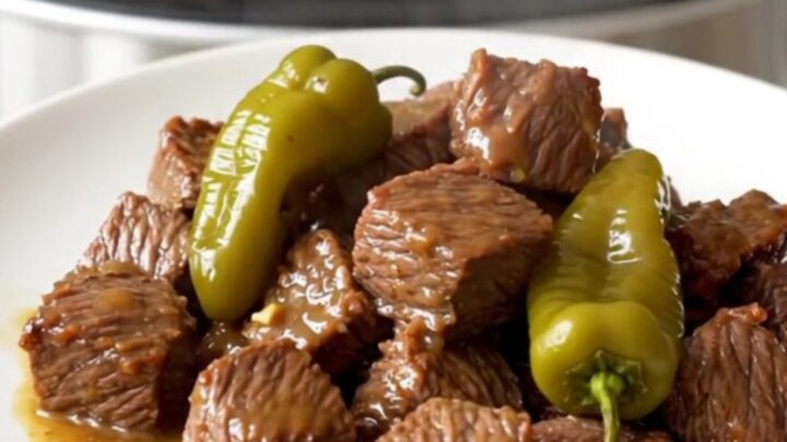 A close-up of tender beef cubes in a rich, buttery sauce with whole pepperoncini, served on a clean white plate.