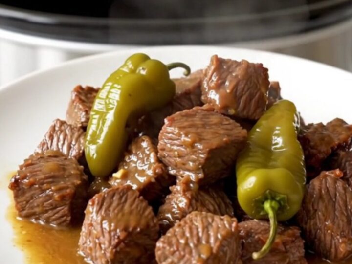 A close-up of tender beef cubes in a rich, buttery sauce with whole pepperoncini, served on a clean white plate.