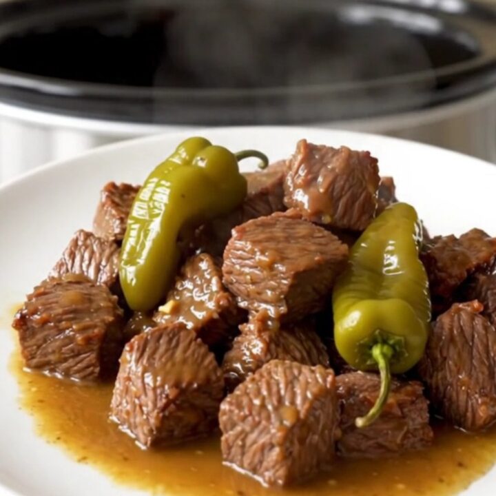 A close-up of tender beef cubes in a rich, buttery sauce with whole pepperoncini, served on a clean white plate.