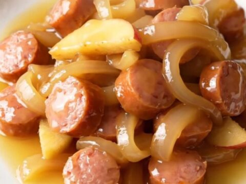 A close-up view of sliced chicken sausage, apples, and onions in a slow cooker, looking warm and savory.