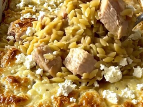 A top-down view of a rectangular baking dish filled with raw orzo, chicken pieces, and lemon broth