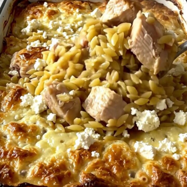 A top-down view of a rectangular baking dish filled with raw orzo, chicken pieces, and lemon broth