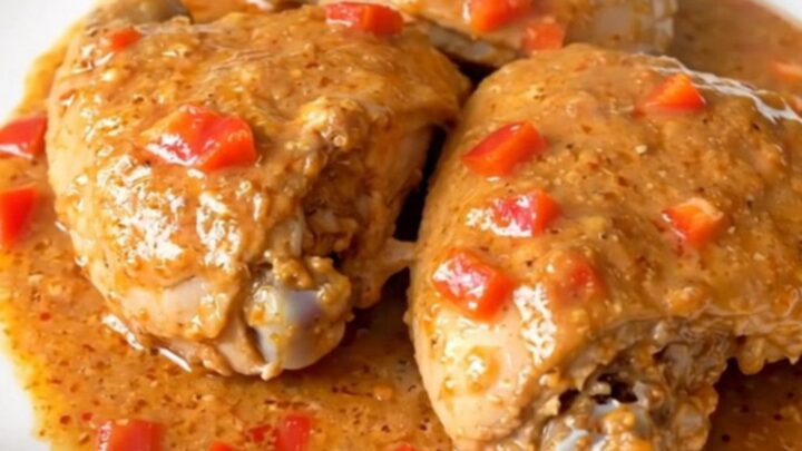 A close-up of tender chicken thighs coated in a rich, creamy pepper jelly sauce in a slow cooker.