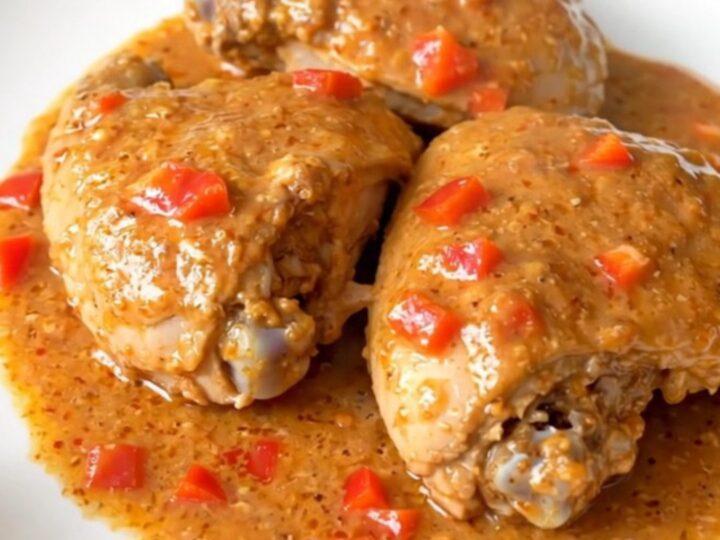 A close-up of tender chicken thighs coated in a rich, creamy pepper jelly sauce in a slow cooker.
