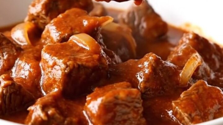 A close-up of tender beef cubes in a rich red chile sauce inside a white bowl.