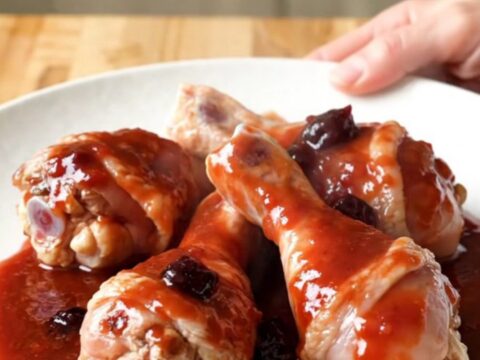 Close up of slow cooker grape jelly drumsticks with a glossy purple sauce in a white ceramic insert.