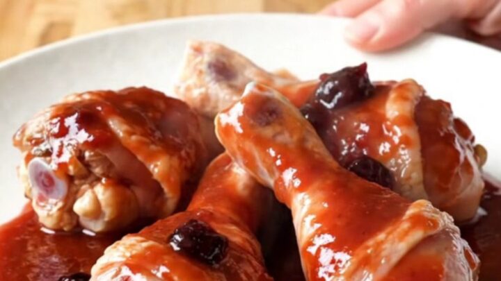 Close up of slow cooker grape jelly drumsticks with a glossy purple sauce in a white ceramic insert.