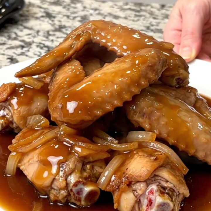 A top-down view of raw turkey wing sections being placed into a black slow cooker insert on a granite countertop.