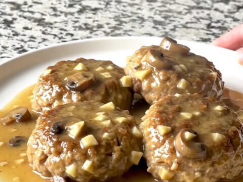 A close-up of a slow cooker filled with turkey patties smothered in a thick, creamy mushroom gravy.