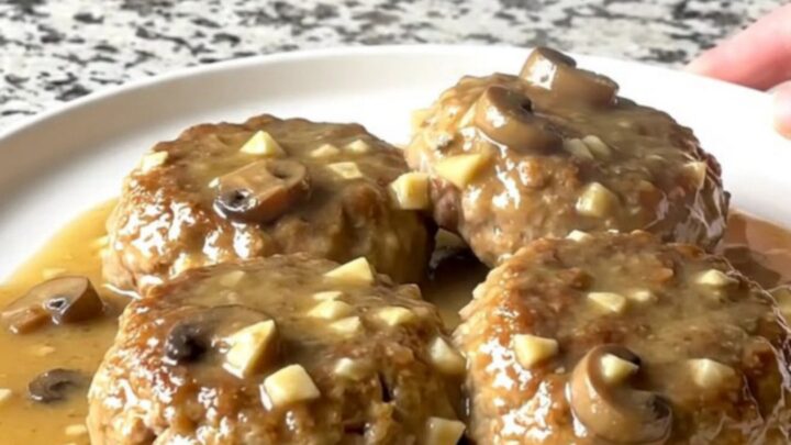 A close-up of a slow cooker filled with turkey patties smothered in a thick, creamy mushroom gravy.