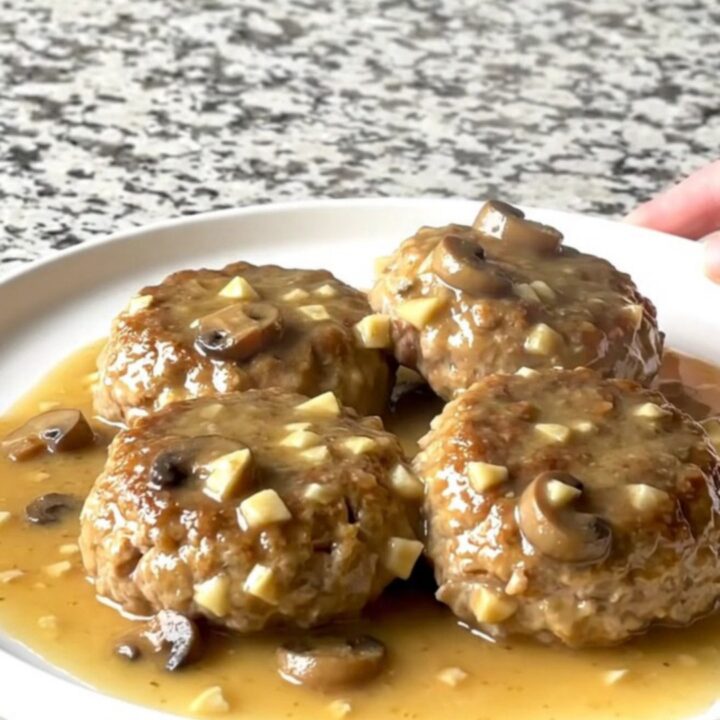 A close-up of a slow cooker filled with turkey patties smothered in a thick, creamy mushroom gravy.