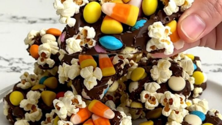 A top-down view of Halloween popcorn bark on a dark baking sheet with scattered candy corn and orange chocolates.