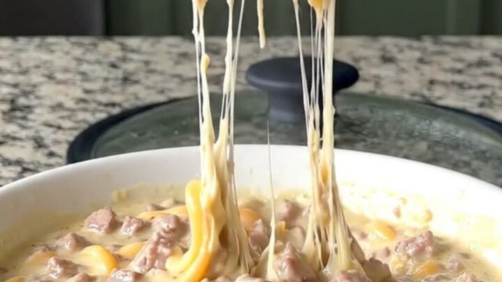 A warm, creamy Italian sub dip in a black slow cooker, topped with melted provolone and peppers.