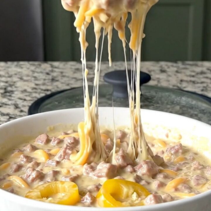 A warm, creamy Italian sub dip in a black slow cooker, topped with melted provolone and peppers.