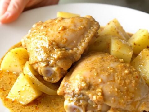 A stainless steel slow cooker filled with raw bone-in chicken thighs, potato cubes, and onion wedges.